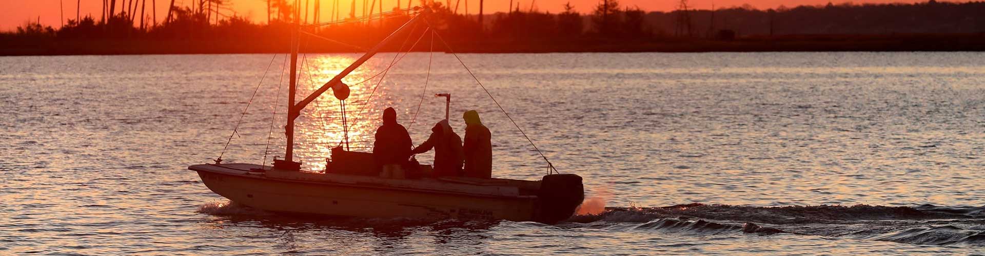A small boat with watermen glides across the water during a vibrant sunset.