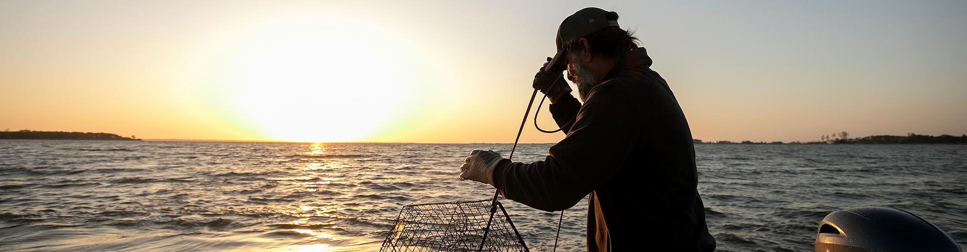 A man stands on a boat, casting a net into the water, engaged in fishing activities.